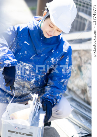 A female painter prepares the roller by placing it between the solvents. 137749775