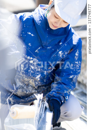 A female painter prepares the roller by placing it between the solvents. 137749777