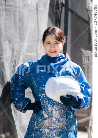 一位活躍在建築業的女工匠。一位身穿沾滿油漆的工作服、微笑的女油漆工。 一位活躍在建築業的女工匠。一位身穿沾滿油漆的工作服、微笑的女油漆工。 137749788