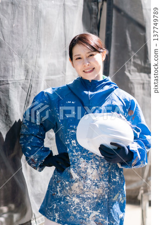 A female craftswoman active in the construction industry. A female painter smiling in her paint-stained work clothes. A female craftswoman active in the construction industry. A female painter smiling in her paint-stained work clothes. 137749789