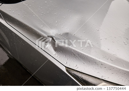 Close-up of a dented silver vehicle hood with chipped paint and water droplets after rain 137750444