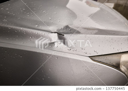 Close-up of a dented silver vehicle hood with chipped paint and water droplets after rain 137750445
