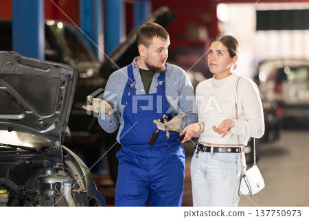 female customer of a car service consults with a mechanic female customer of a car service consults with a mechanic 137750973