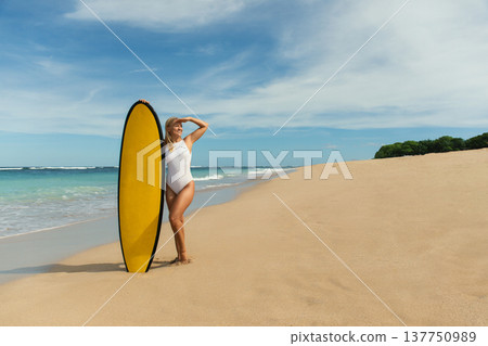 Surfer poses on a beautiful beach with golden sand and calm waves Surfer poses on a beautiful beach with golden sand and calm waves 137750989