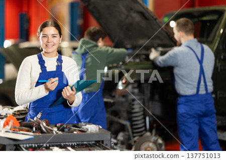 Female car service worker keeps records of work performed by auto mechanics in car service station - makes notes on paper Female car service worker keeps records of work performed by auto mechanics in car service station - makes notes on paper 137751013