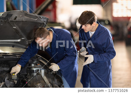 Two auto mechanics work together to diagnose an engine under the hood of a car in repair shop Two auto mechanics work together to diagnose an engine under the hood of a car in repair shop 137751026