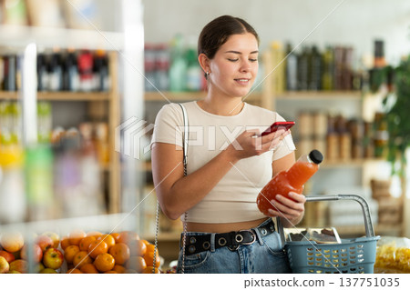 European young woman customer at shop scans QR code on grapefruit juice bottle using phone camera European young woman customer at shop scans QR code on grapefruit juice bottle using phone camera 137751035