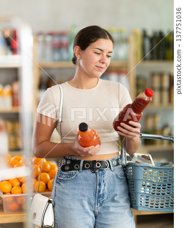 Girl hold packages bottles and choose consider juice in store Girl hold packages bottles and choose consider juice in store 137751036