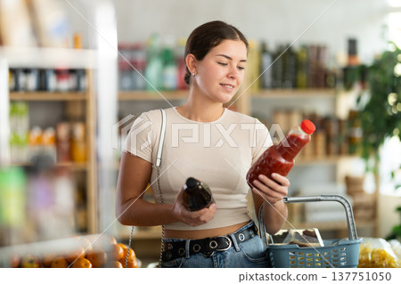 Girl hold packages bottles and choose consider juice in store Girl hold packages bottles and choose consider juice in store 137751050
