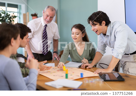 Elderly professor playing board game with students at table 137751266