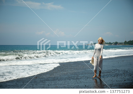 Woman strolls on a black sand beach near the ocean Woman strolls on a black sand beach near the ocean 137751273