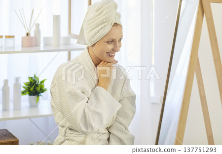 Happy beautiful woman enjoys appearance applying cosmetcs, cream product to face looking in mirror Happy beautiful woman enjoys appearance applying cosmetcs, cream product to face looking in mirror 137751293