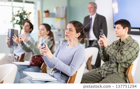 Young female student scans QR code or takes photo, teacher in background Young female student scans QR code or takes photo, teacher in background 137751294