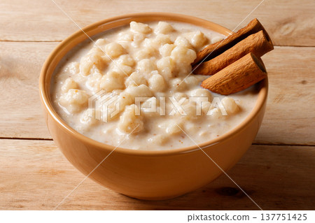 Mungunza, or Brazilian creamy canjica, served in a ceramic bowl and decorated with cinnamon sticks, placed alone on a light wood table Mungunza, or Brazilian creamy canjica, served in a ceramic bowl and decorated with cinnamon sticks, placed alone on a light wood table 137751425