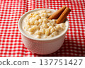Canjica or mungunza creme, a traditional Brazilian dessert made with white corn, served in a white bowl with cinnamon sticks on a red checkered tablecloth 137751427