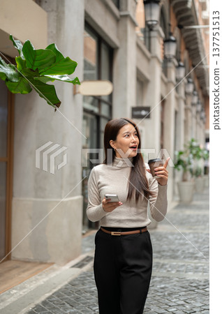 Asian woman holding coffee and phone looking around pointing as walking in shopping mall or market. 137751513