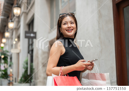 Pretty asian woman holding phone and shopping bags walking or standing sideway in a mall or market. Pretty asian woman holding phone and shopping bags walking or standing sideway in a mall or market. 137751550