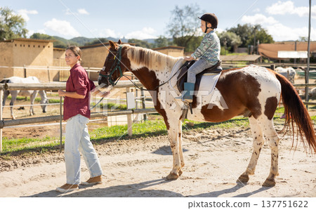 Happy mother leads horse with his son on it - walk around horse farm Happy mother leads horse with his son on it - walk around horse farm 137751622