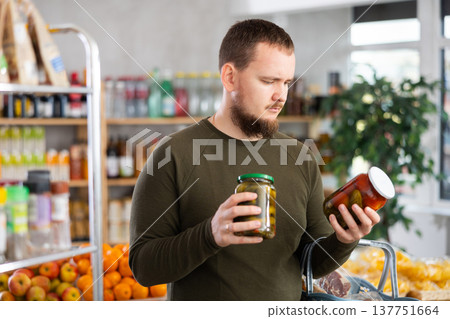 Man chooses pickled cucumbers and tomatoes in the store Man chooses pickled cucumbers and tomatoes in the store 137751664