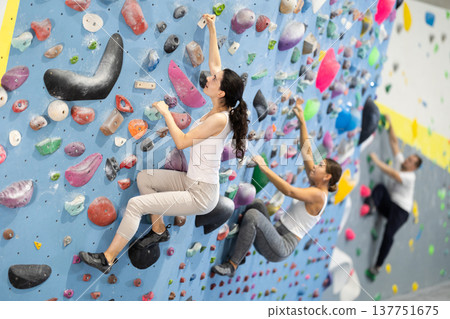 Motivated young girl climbing without ropes and harnesses on artificial bouldering wall in fitness center Motivated young girl climbing without ropes and harnesses on artificial bouldering wall in fitness center 137751675