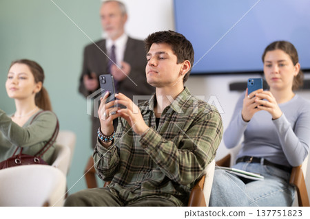 Young guy scanning QR-code with mobile devices during presentation Young guy scanning QR-code with mobile devices during presentation 137751823