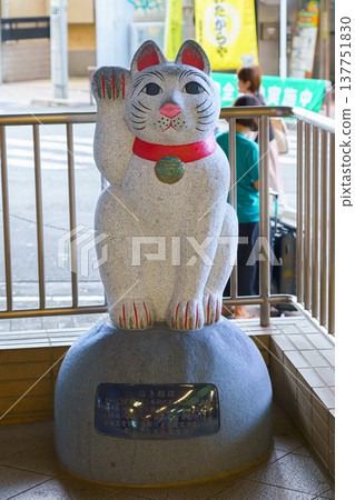 Tokyo, Japan - Sep 30 2024, vertical view of the sculpture of the white cat Maneki Neko on the street near the entrance to the subway station, with people on background, at daytime, Tokyo, Japan Tokyo, Japan - Sep 30 2024, vertical view of the sculpture of the white cat Maneki Neko on the street near the entrance to the subway station, with people on background, at daytime, Tokyo, Japan 137751830