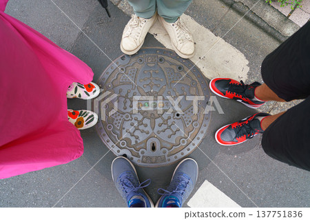 Tokyo, Japan - Sep 30 2024, A close-up view of a manhole surrounded by the feet of a family of four, at daytime, Tokyo, Japan Tokyo, Japan - Sep 30 2024, A close-up view of a manhole surrounded by the feet of a family of four, at daytime, Tokyo, Japan 137751836