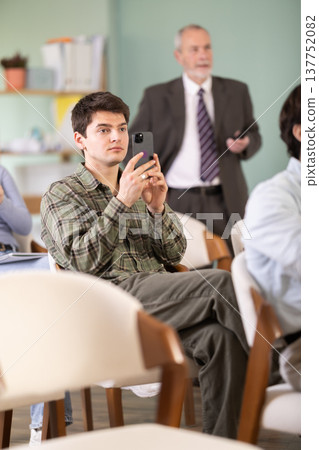 Young male student scans QR code or takes photo, teacher in background 137752082