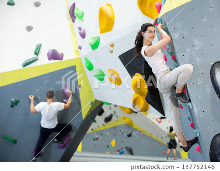 Motivated young girl climbing without ropes and harnesses on artificial bouldering wall in fitness center Motivated young girl climbing without ropes and harnesses on artificial bouldering wall in fitness center 137752146