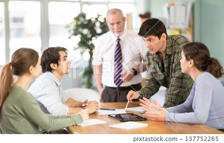 Students solving issues at the table in front of the teacher Students solving issues at the table in front of the teacher 137752265
