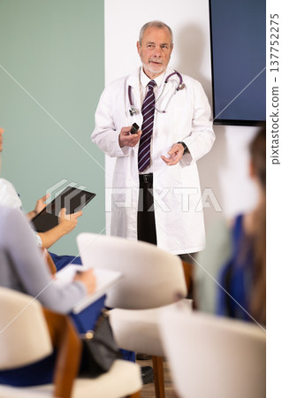 Senior medical professor speaking to students in blue overalls 137752275