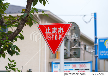 Tokyo, Japan - Sep 30 2024, A close-up view of a triangular red traffic stop sign hanging over the road, with building facades and an cloudy sky in the background, Tokyo, Japan Tokyo, Japan - Sep 30 2024, A close-up view of a triangular red traffic stop sign hanging over the road, with building facades and an cloudy sky in the background, Tokyo, Japan 137752280