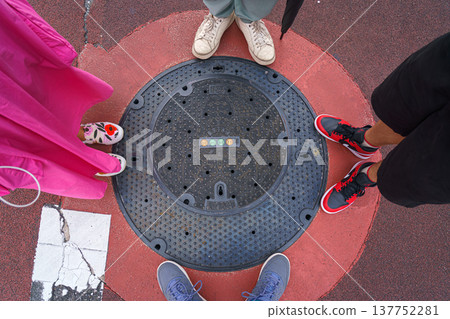 Tokyo, Japan - Sep 30 2024, A close-up view of a manhole surrounded by the feet of a family of four, at daytime, Tokyo, Japan Tokyo, Japan - Sep 30 2024, A close-up view of a manhole surrounded by the feet of a family of four, at daytime, Tokyo, Japan 137752281