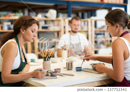 Pottery workers paint ceramic plates together at table Pottery workers paint ceramic plates together at table 137752341