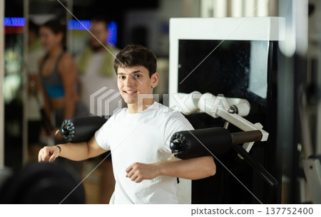 Guy in gym performs exercises for arm muscles using simulators and fitness center equipment. 137752400