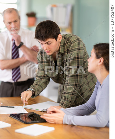 Students solving problems at table with teacher in background 137752407