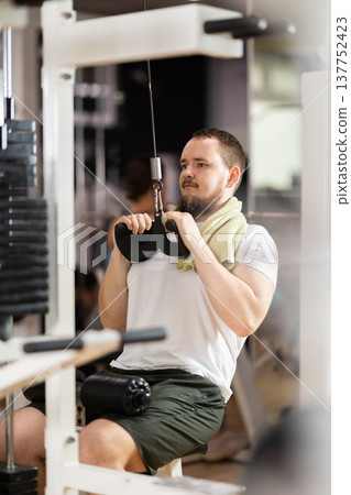 Man in gym performs exercises for arm muscles using cable crossover machine and pull weighted rope Man in gym performs exercises for arm muscles using cable crossover machine and pull weighted rope 137752423