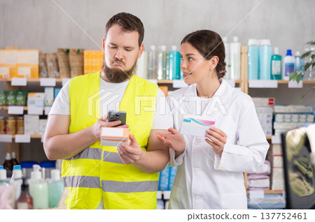 Laborer man builder in pharmacy scans QR code on pills box, pharmacist offer help for customer Laborer man builder in pharmacy scans QR code on pills box, pharmacist offer help for customer 137752461