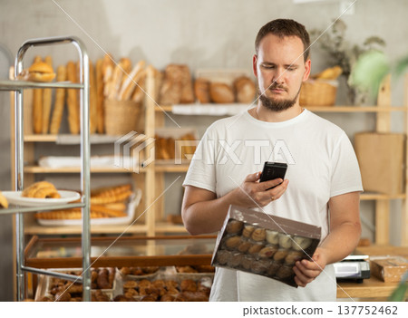 Man customer at bakery scans QR code on cookie package using phone camera Man customer at bakery scans QR code on cookie package using phone camera 137752462