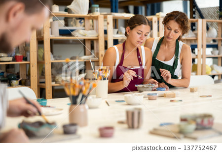 During master class, student paints clay vessel under guidance of female teacher. 137752467