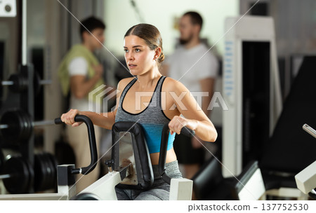Girl in gym performs exercises for arm muscles using simulators and fitness center equipment. 137752530