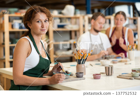 During workshop at master class, female employee paints clay vessel plate During workshop at master class, female employee paints clay vessel plate 137752532