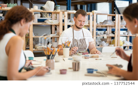 Pottery workers paint ceramic plates together at table 137752544