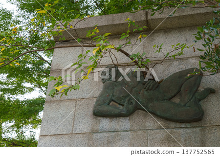 Tokyo, Japan - Sep 30 2024, close-up view of a wall with a metal bas-relief in the form of a reclining man, from which a tree grows, in the cemetery at Gotokuji Temple, without people, Tokyo, Japan 137752565