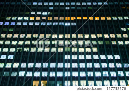 Tokyo, Japan, panoramic view of the facade of an office building at night with lights on in most windows of offices where people work 137752576