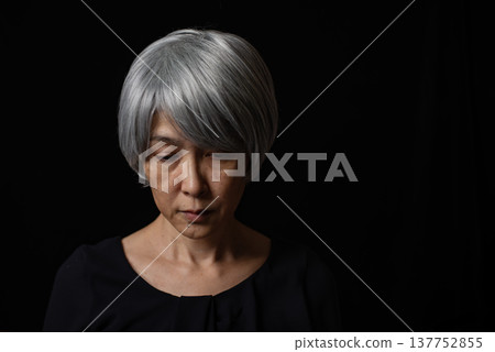 A senior woman with white hair lowers her eyes sadly. A senior woman with white hair lowers her eyes sadly. 137752855