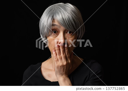 A senior woman with white hair covers her mouth with her hand in surprise. A senior woman with white hair covers her mouth with her hand in surprise. 137752865