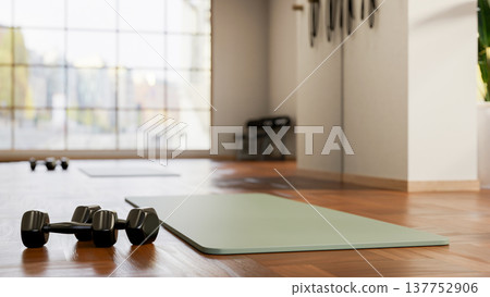 Black dumbbells and a yoga mat on wooden tiles floor across glass wall in fitness gym exercise room. Black dumbbells and a yoga mat on wooden tiles floor across glass wall in fitness gym exercise room. 137752906