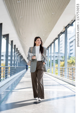 Full body asian woman student office worker holding tablet walking with hand in pocket on footbridge Full body asian woman student office worker holding tablet walking with hand in pocket on footbridge 137753053