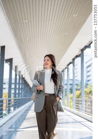 Pretty asian woman student office worker holding tablet as walking with hand in pocket on footbridge Pretty asian woman student office worker holding tablet as walking with hand in pocket on footbridge 137753055